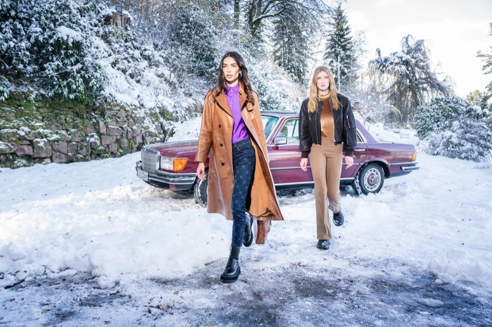 Zwei Models gehen mit einem Oldtimer eine verschneite Straße entlang, Angels-Jeans-Kampagne HW24 in Freudenstadt