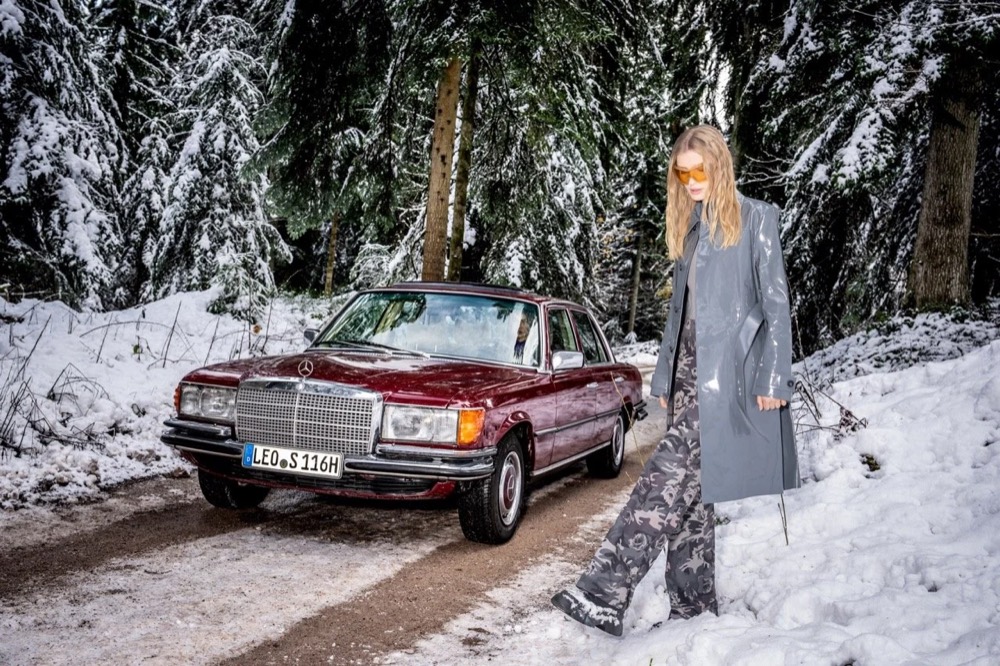 Model in einem verschneiten Wald neben einem roten Oldtimer, Angels-Jeans-Kampagne HW24 in Freudenstadt