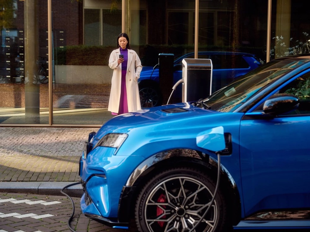Frau schaut an einer öffentlichen Ladestation auf ihr Handy, Shooting für Athlon Car Lease in Amsterdam