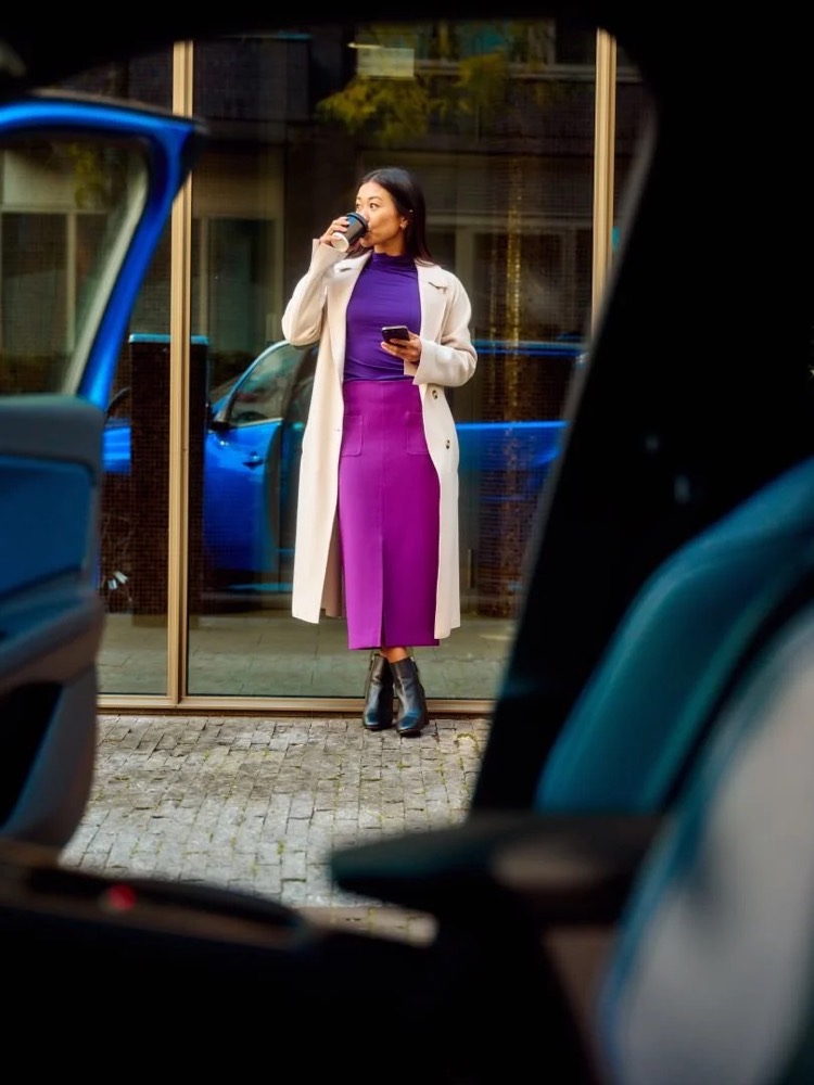 Frau trinkt Kaffee, während ihr Auto lädt, Shooting für Athlon Car Lease in Amsterdam