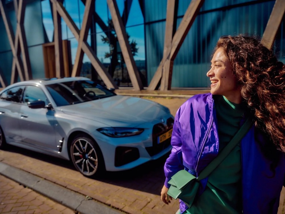 Lächelnde Frau in der Stadt, ihr Auto im Hintergrund, Shooting für Athlon Car Lease in Amsterdam
