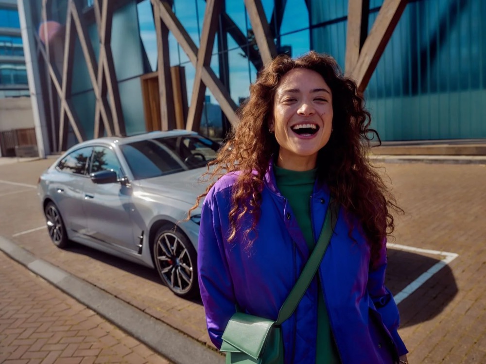 Lächelnde Frau im urbanen Umfeld, Auto im Hintergrund, Shooting für Athlon Car Lease in Amsterdam