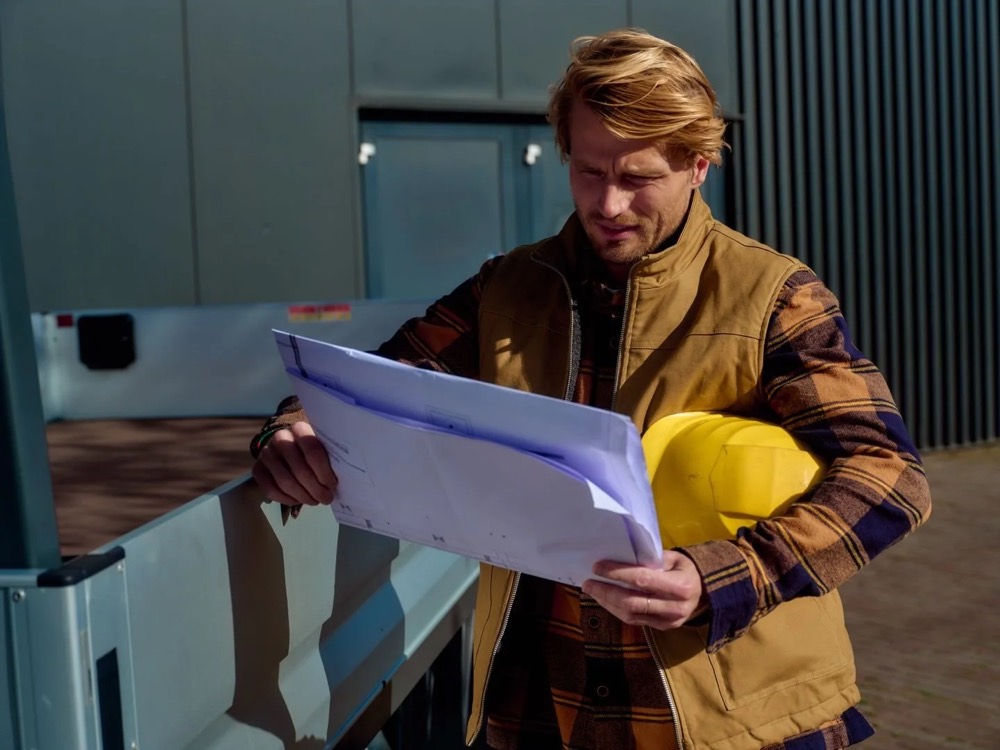 Bauarbeiter mit gelbem Helm prüft Pläne neben einem Transporter, Shooting für Athlon Car Lease in Amsterdam