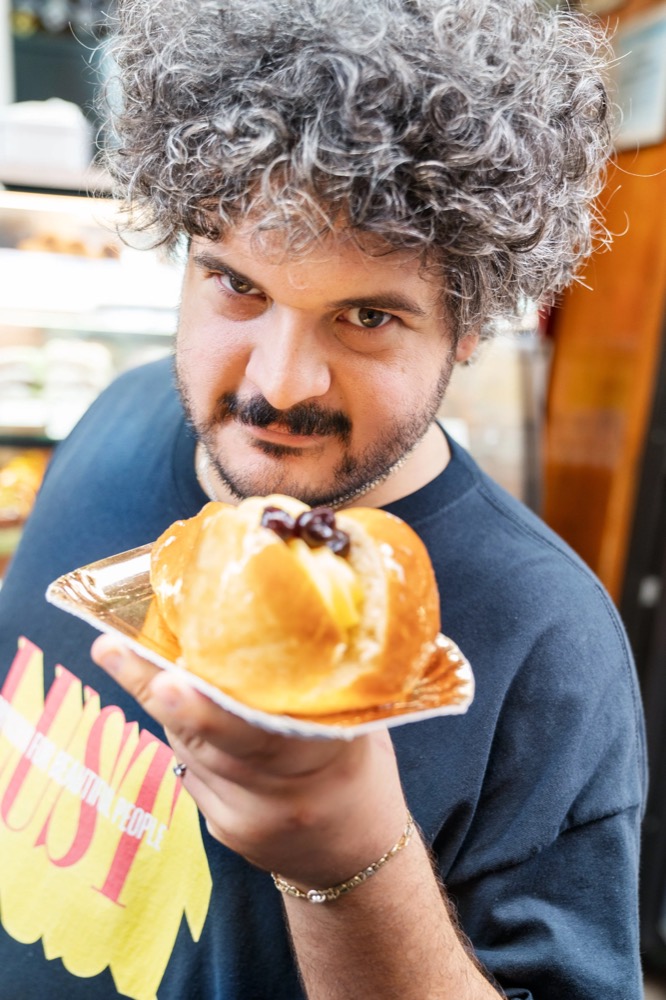 Model mit Locken beißt in eine Sfogliatella, Drykorn-Kampagne FS/SS 23 in Neapel