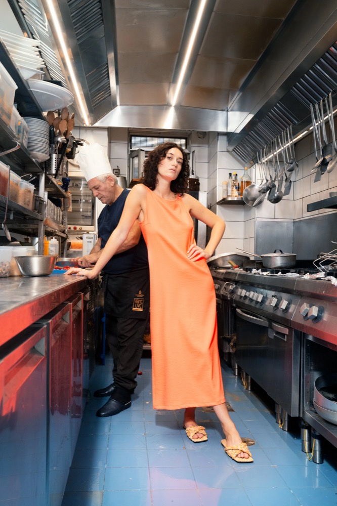 Model im orangefarbenen Kleid in einer Restaurantküche, Drykorn-Kampagne FS/SS 23 in Neapel