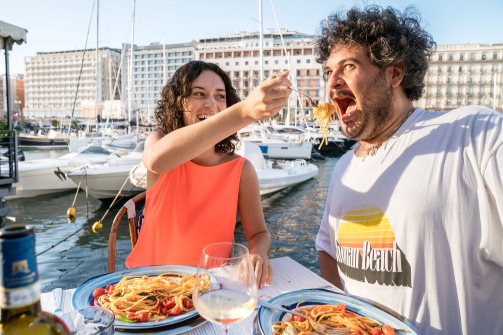 Paar isst an einem Tisch am Hafen, Drykorn-Kampagne FS/SS 23 in Neapel