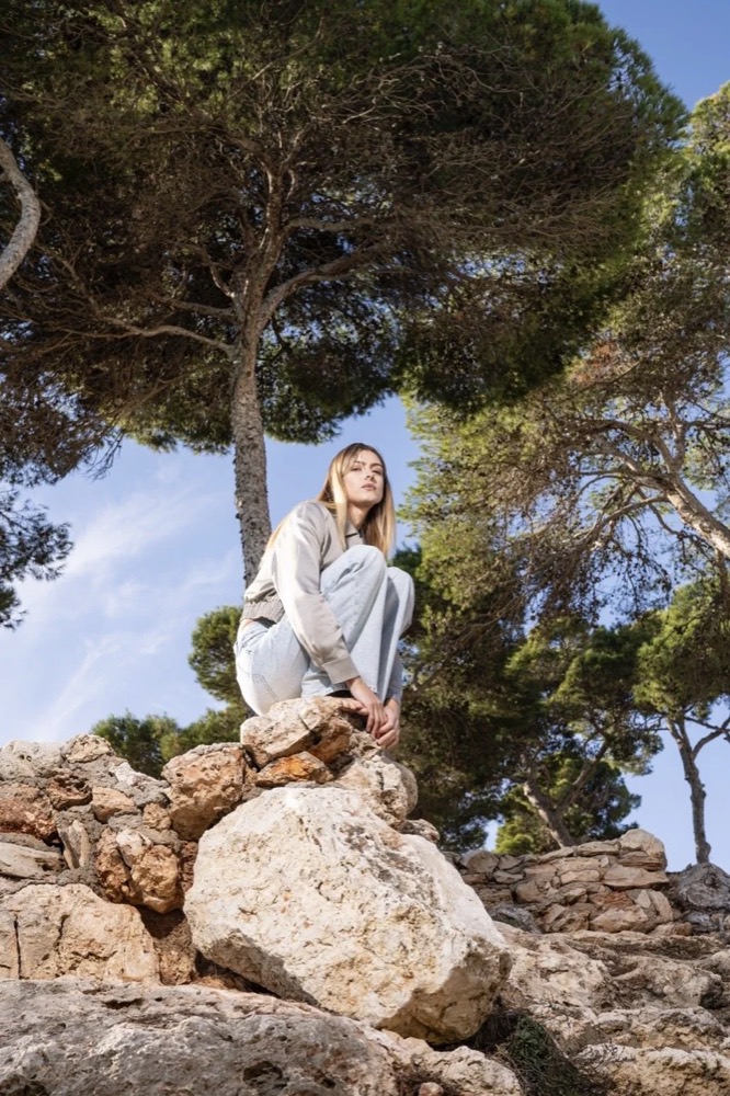 Model sitzt auf Felsen unter Pinien, Drykorn-Kampagne FS/SS 24 Teil II auf Mallorca