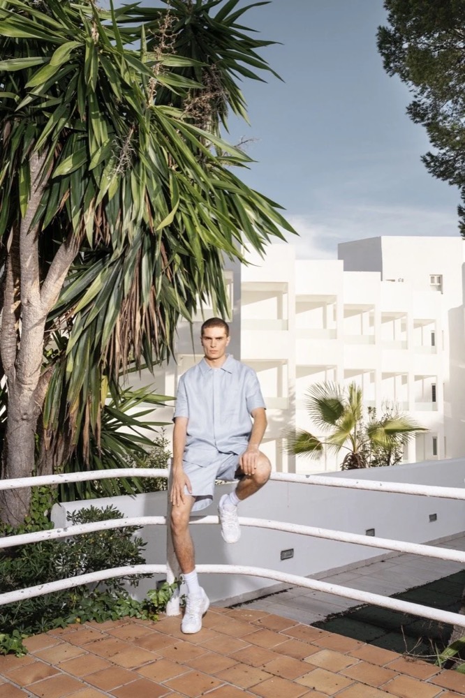 Model auf einem weißen Balkongeländer unter einer Palme, Drykorn-Kampagne FS/SS 24 Teil II auf Mallorca