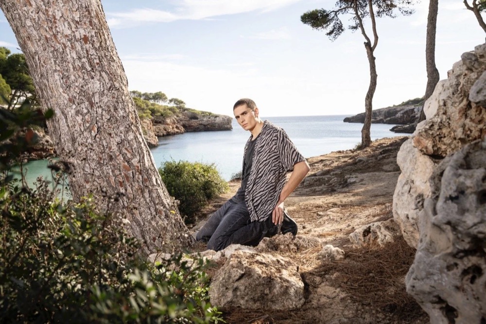 Model sitzt auf Felsen am Meer, Drykorn-Kampagne FS/SS 24 Teil II auf Mallorca