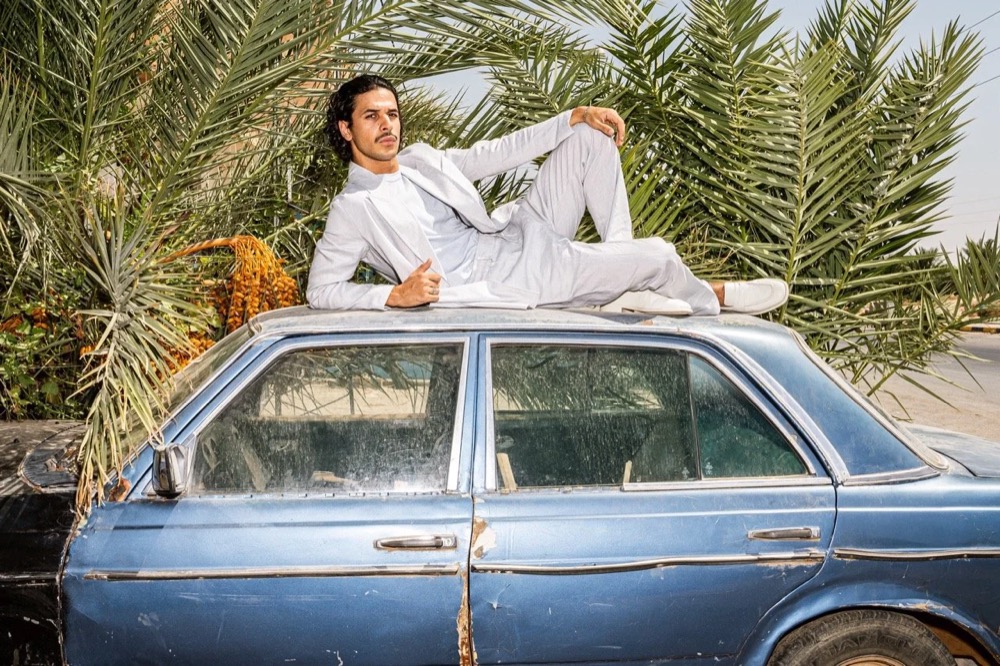 Model liegt auf dem Dach eines blauen Mercedes unter Palmen, Drykorn-Kampagne FS/SS 24 in Tozeur, Tunesien