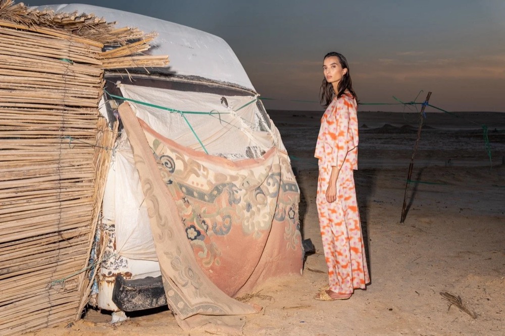 Model im langen Kleid vor einem rostigen Wohnwagen, Drykorn-Kampagne FS/SS 24 in Tozeur, Tunesien