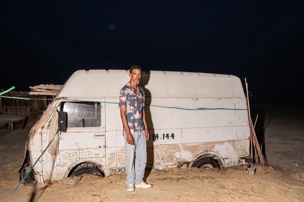 Model nachts neben einem alten weißen Transporter, Drykorn-Kampagne FS/SS 24 in Tozeur, Tunesien