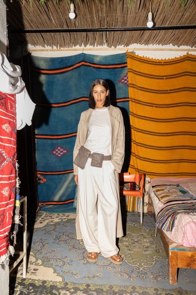 Model in Creme in einem Stoffladen mit gestreiften Teppichen, Drykorn-Kampagne FS/SS 24 in Tozeur, Tunesien