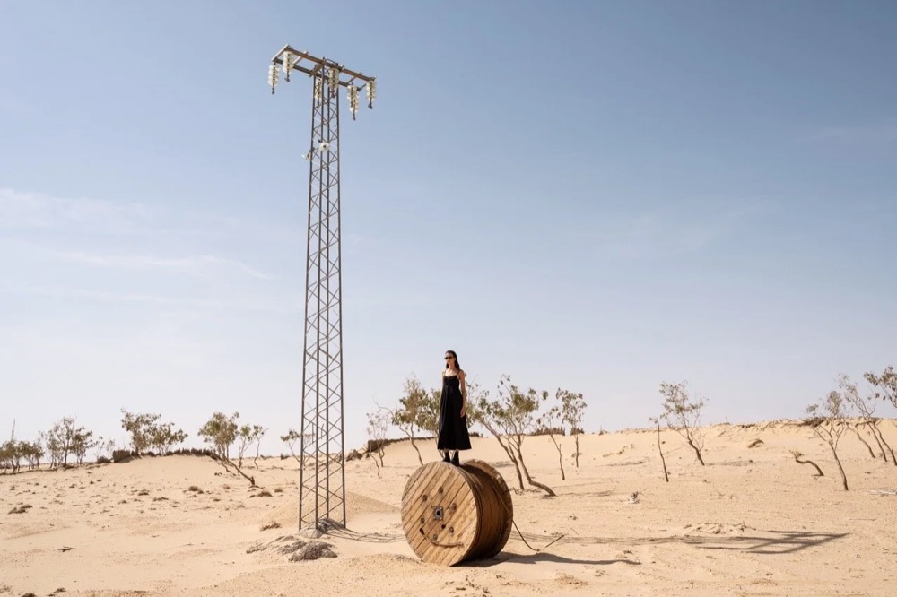 Model auf einem Heuballen neben einem Strommast in der Wüste, Drykorn-Kampagne FS/SS 24 in Tozeur, Tunesien