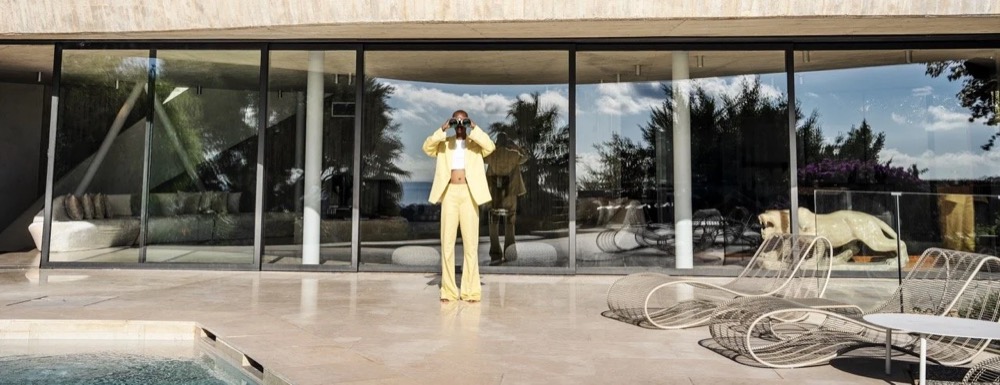 Model in Gelb an einer modernistischen Villa mit Pool, Drykorn-Kampagne FS/SS25 auf Ibiza