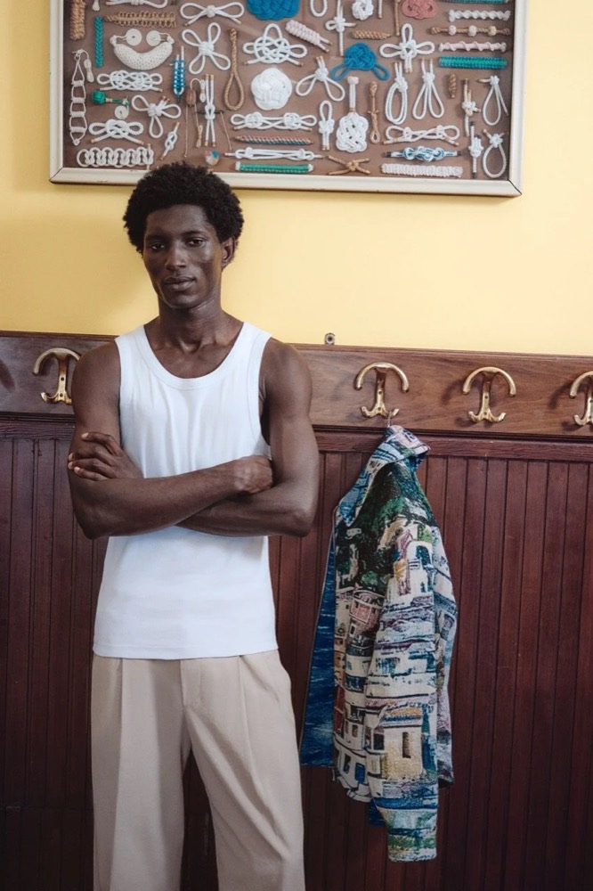 Model im weißen Tanktop vor einer Holztür, Drykorn-Kampagne FS/SS26 in Genua