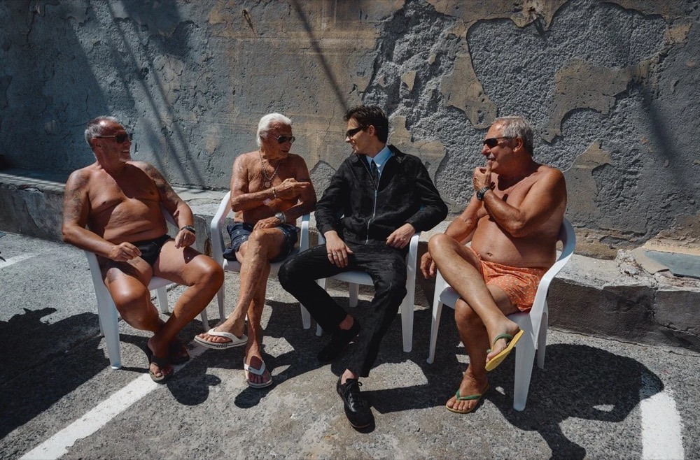 Ältere Männer sitzen mit einem Model auf einem Steg, Drykorn-Kampagne FS/SS26 in Genua