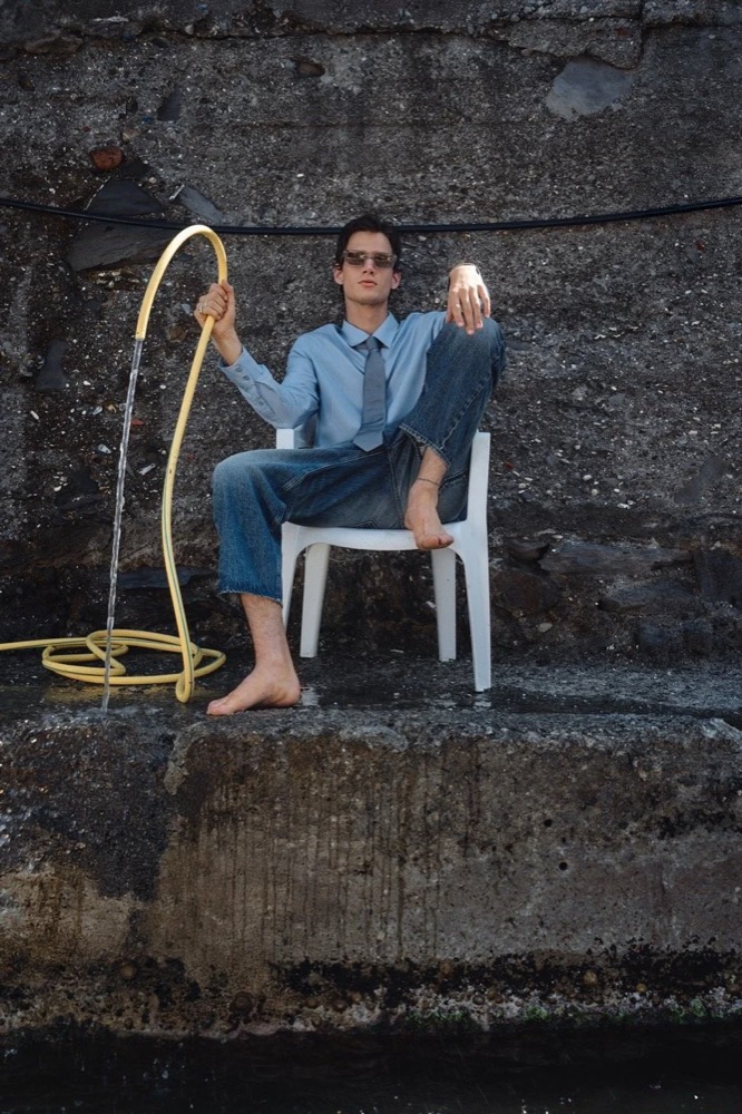 Model in Denim auf einem Stuhl mit aufgerolltem Tau, Drykorn-Kampagne FS/SS26 in Genua