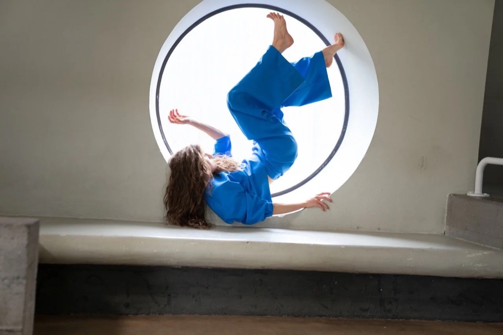 Model in Blau liegt in einem runden Fenster, Drykorn-Kampagne HW/AW 22