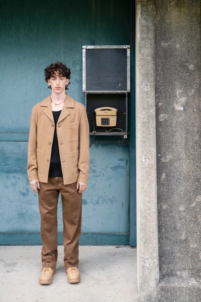 Model in kamelfarbener Jacke vor einer verwitterten blauen Wand, Drykorn-Kampagne HW/AW 22