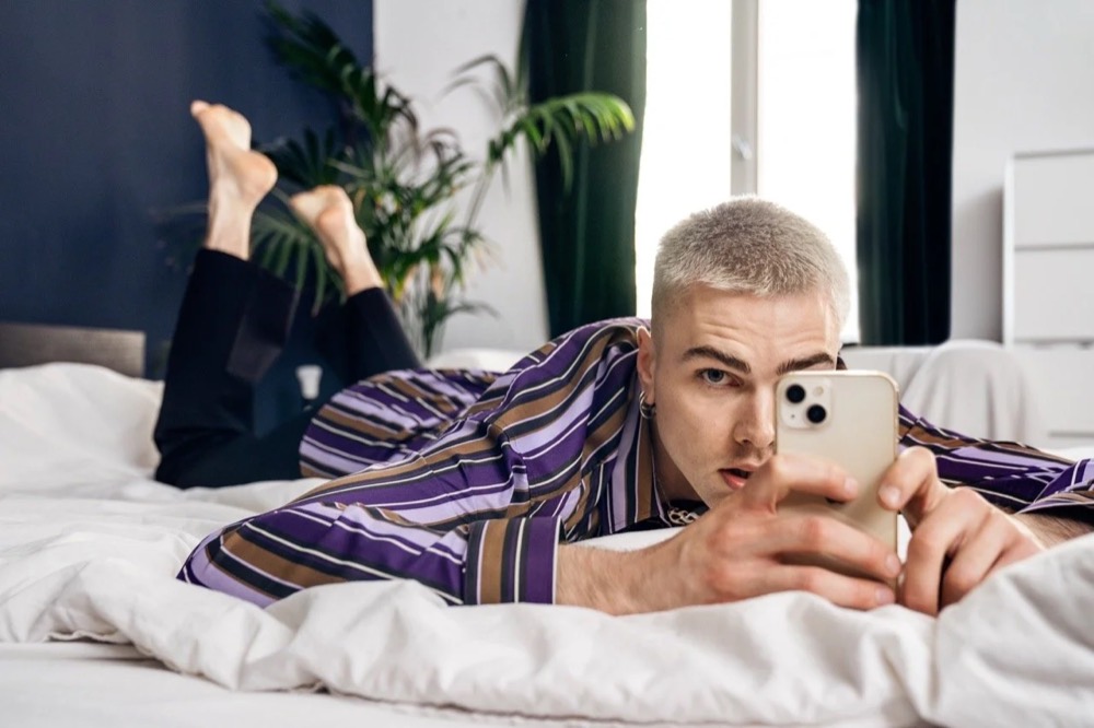 Model im gestreiften Hemd liegt mit Handy auf einem Bett, Drykorn-Kampagne HW/AW 22