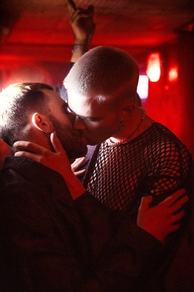 Zwei Männer küssen sich in einer rot beleuchteten Bar, Drykorn-Kampagne HW/AW 22