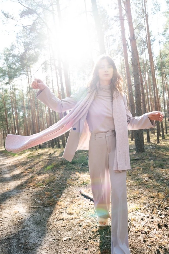 Model in hellem Strick in einem sonnigen Kiefernwald, Drykorn-Kampagne HW/AW 22