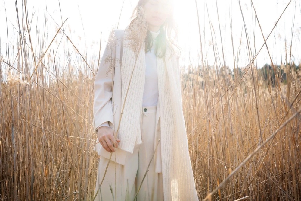 Model in Weiß in einem Feld aus trockenem Schilf, Drykorn-Kampagne HW/AW 22