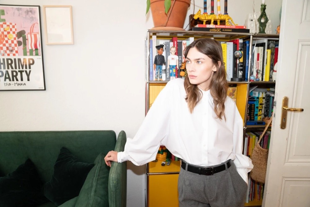 Model in weißer Bluse in einem Wohnzimmer, Drykorn-Kampagne HW/AW 22