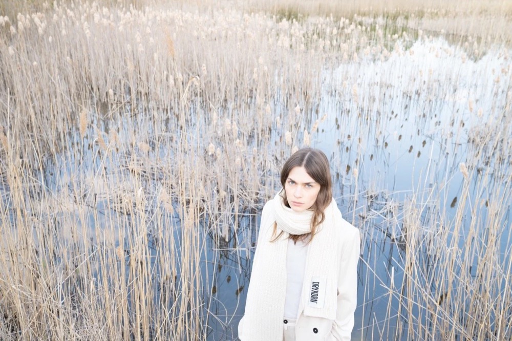 Model in Weiß sitzt auf einem bereiften Feld, Drykorn-Kampagne HW/AW 22