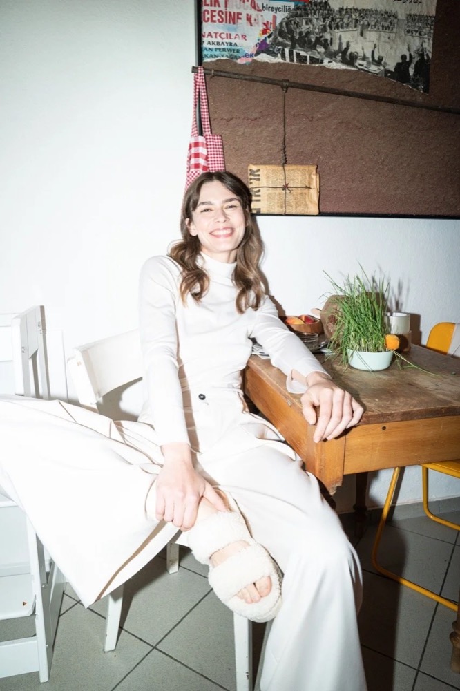 Model in Weiß sitzt auf einem Stuhl in einer Küche, Drykorn-Kampagne HW/AW 22