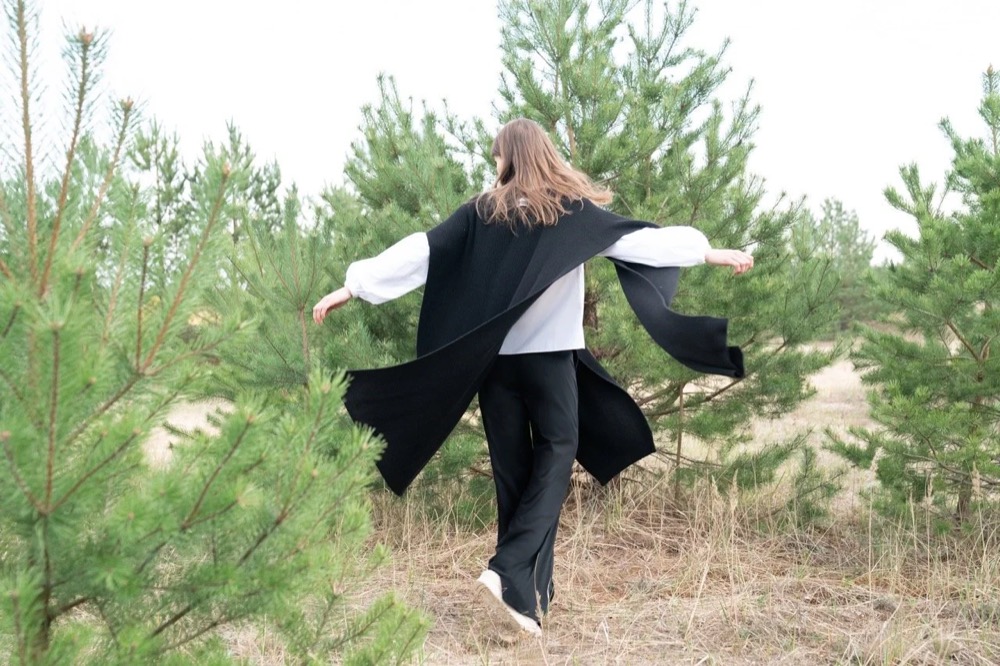 Model im schwarzen Mantel in einem jungen Kiefernwald, Drykorn-Kampagne HW/AW 22