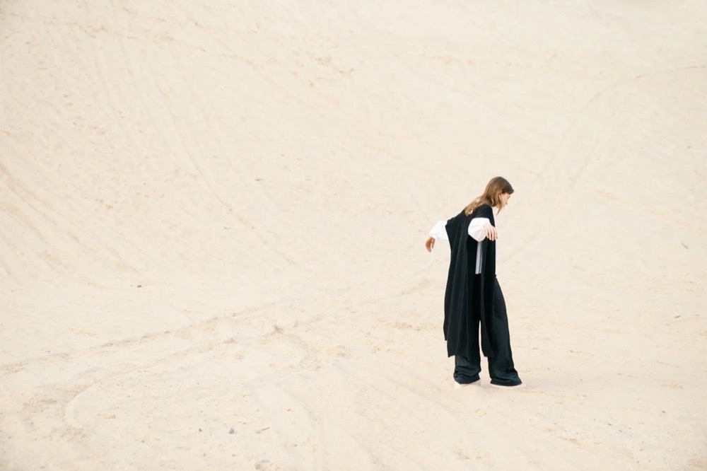 Model in Schwarz in einem hellen, leeren Raum, Drykorn-Kampagne HW/AW 22