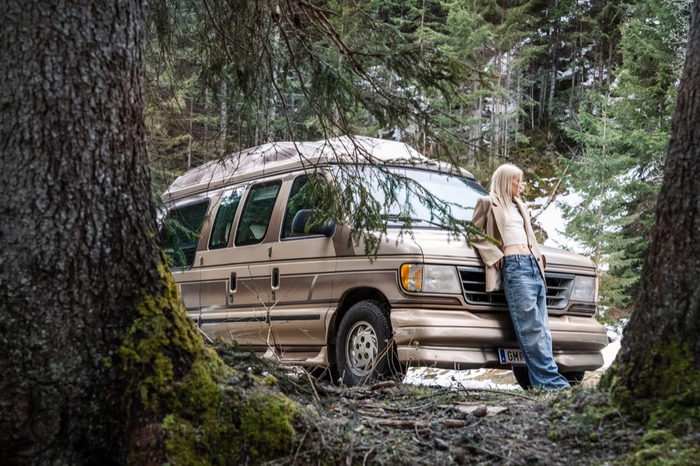 Model neben einem alten Campingbus in einem Wald, Drykorn-Kampagne HW/AW 23 in Bad Gastein