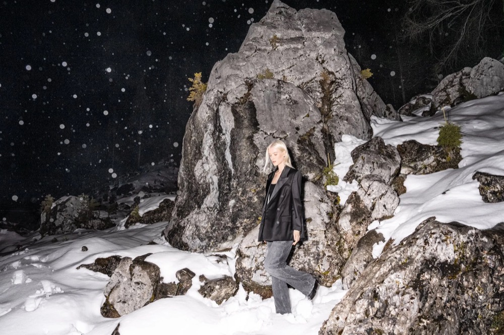Model nachts an einem Felsen im Schnee, Drykorn-Kampagne HW/AW 23 in Bad Gastein