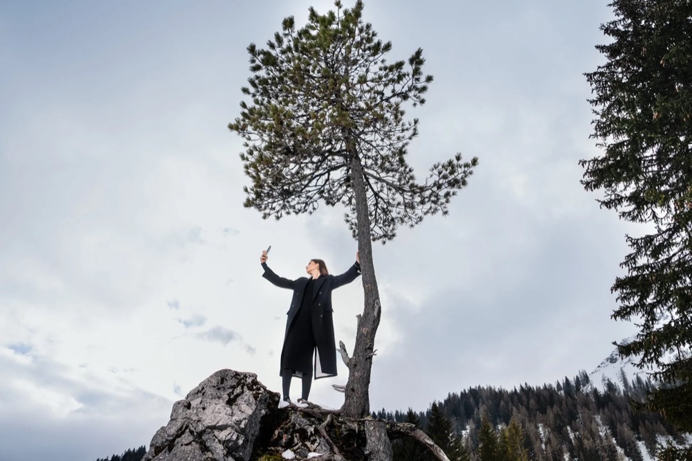 Model unter einer einzelnen Kiefer in den Bergen, Drykorn-Kampagne HW/AW 23 in Bad Gastein