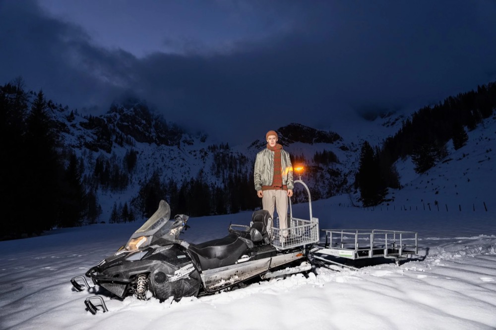 Model auf einem Schneemobil in den Bergen in der Dämmerung, Drykorn-Kampagne HW/AW 23 in Bad Gastein