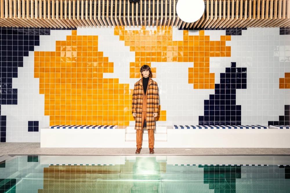 Model an einem Retro-Hallenbad mit gefliestem Wandbild, Drykorn-Kampagne HW/AW 23 in Bad Gastein