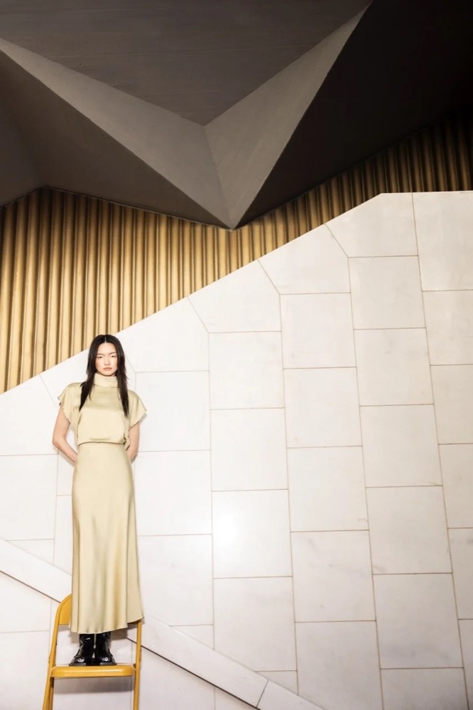 Model im langen cremefarbenen Kleid vor einer hellen Wand, Drykorn-Kampagne HW/AW 24 in einem Theater in Turin