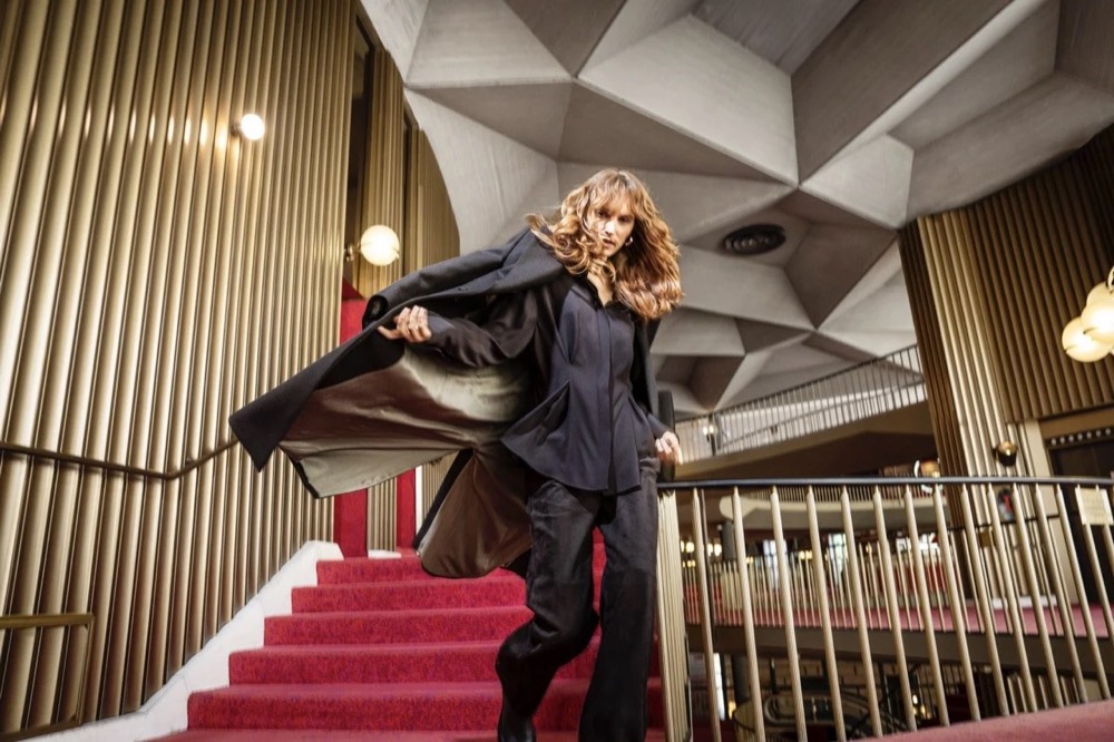 Model auf einer roten Treppe in einem modernistischen Foyer, Drykorn-Kampagne HW/AW 24 in einem Theater in Turin