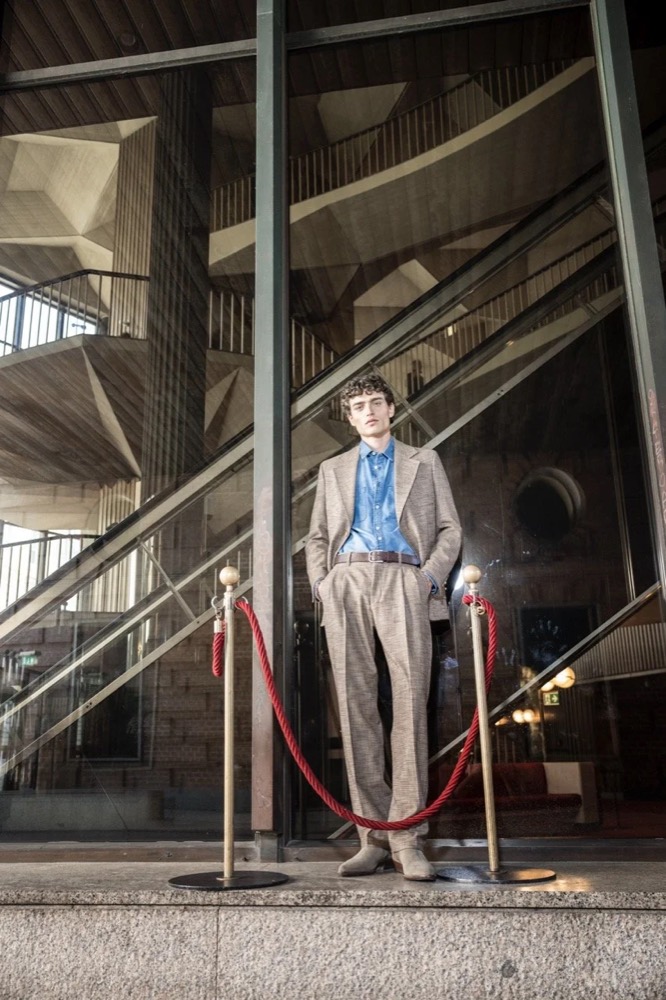 Model im blauen Anzug am Fuß einer Treppe, Drykorn-Kampagne HW/AW 24 in einem Theater in Turin