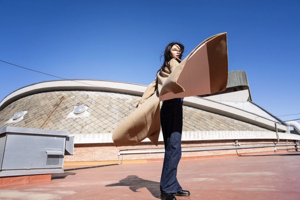 Model auf einem Dach vor einem modernistischen Gebäude und blauem Himmel, Drykorn-Kampagne HW/AW 24 in einem Theater in Turin