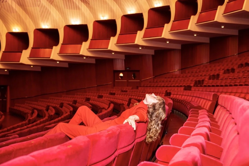 Model liegt quer über roten Theatersesseln, Drykorn-Kampagne HW/AW 24 in einem Theater in Turin