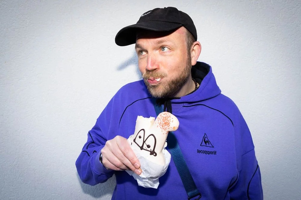 Mann in lila Hoodie und Cap hält ein kleines Plüschtier, Bespoke-Shooting für ING
