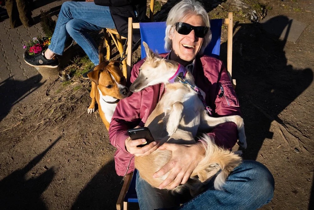 Ältere Frau mit Sonnenbrille sitzt mit ihrem Hund im Freien, Bespoke-Shooting für ING