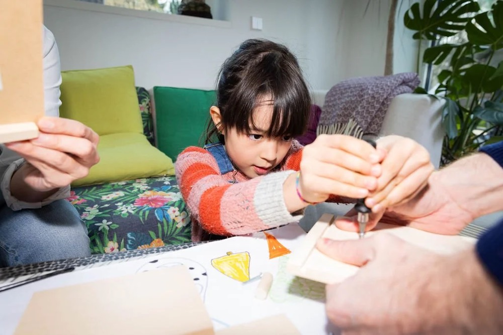 Kind bastelt mit einem Erwachsenen an einem Tisch, Bespoke-Shooting für ING