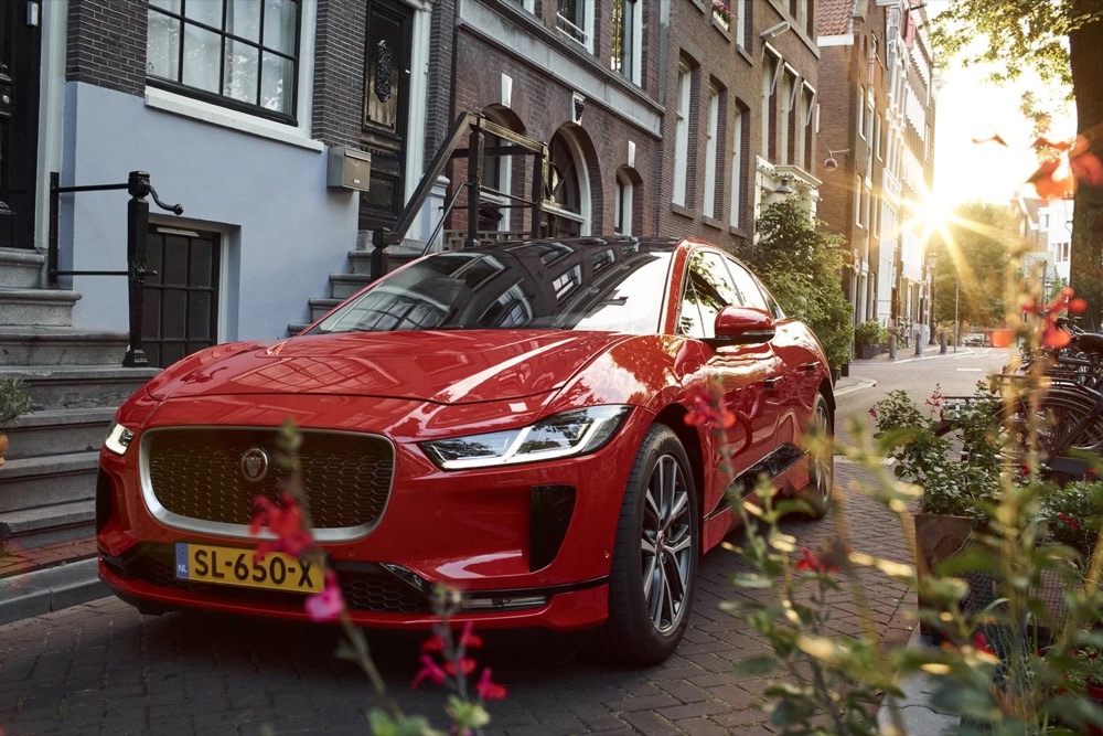 Frontansicht eines roten Jaguar I-PACE vor Amsterdamer Stadthäusern
