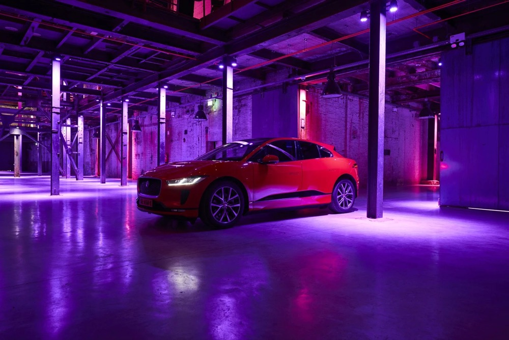 Roter Jaguar I-PACE in einem lila beleuchteten Parkhaus, Totale