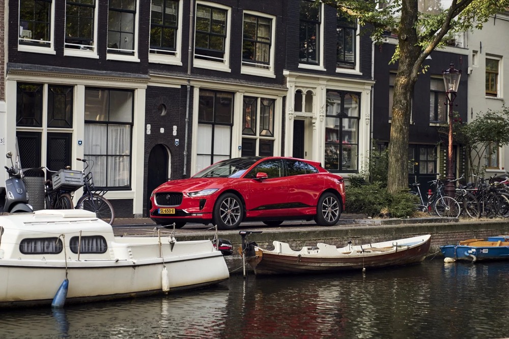 Roter Jaguar I-PACE an einer Gracht mit Booten in Amsterdam