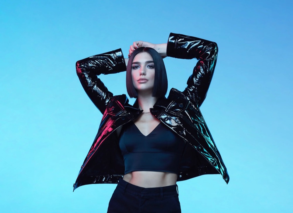 Dua Lipa posiert mit den Händen hinter dem Kopf vor Hellblau, Jaguar The Pace